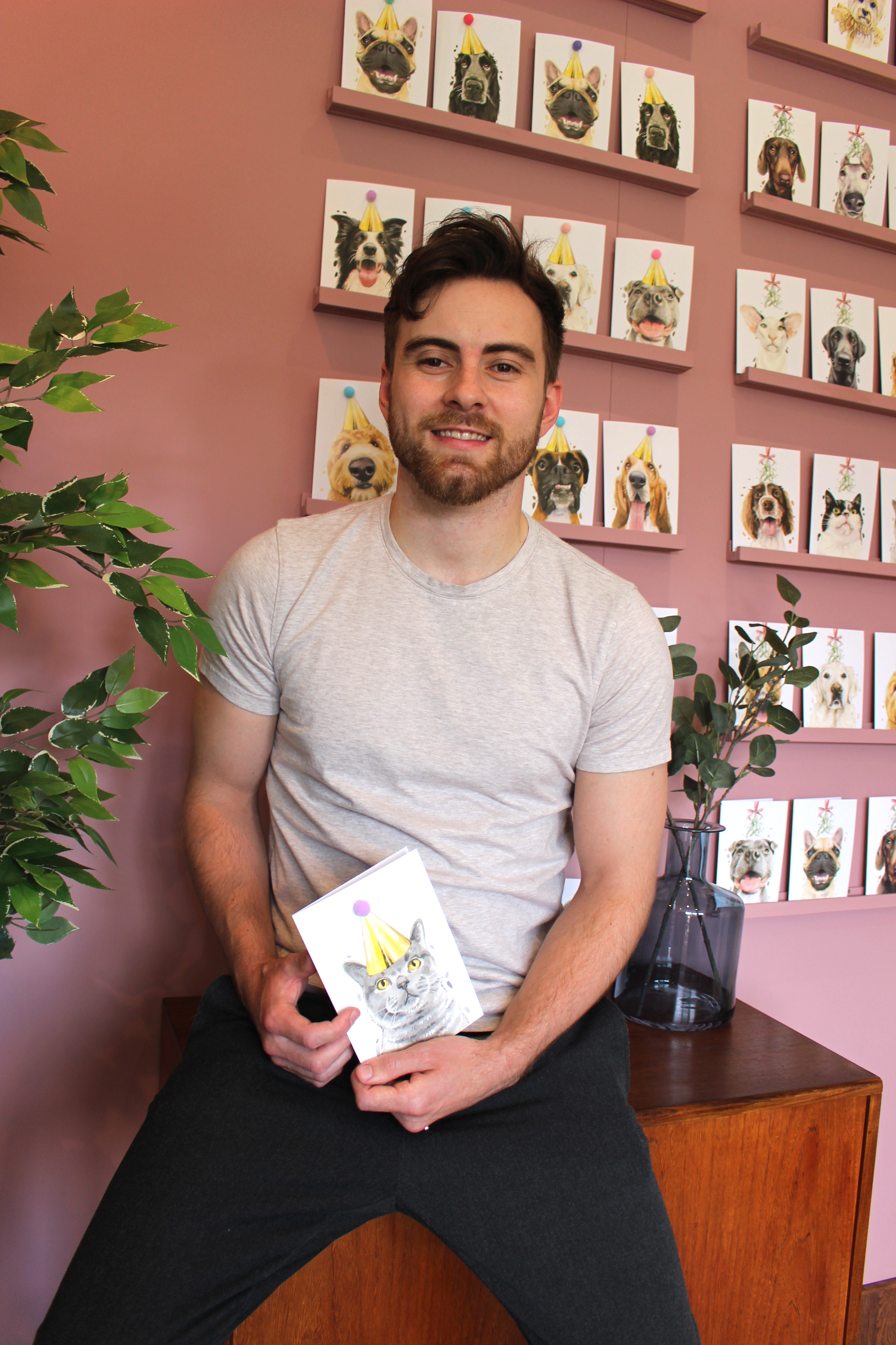 Me, Robert, holding my British Shorthair Cat Pompom Birthday Celebration card, stood in front of a range of my other cards