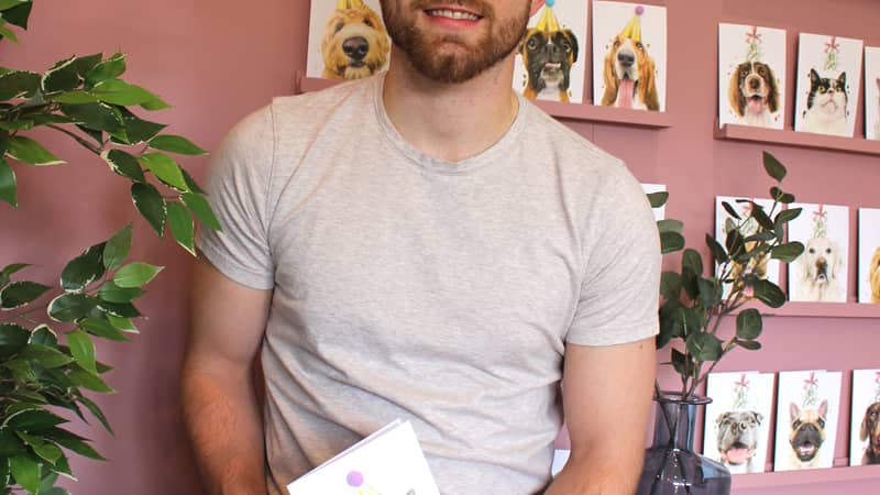 Me, Robert, holding my British Shorthair Cat Pompom Birthday Celebration card, stood in front of a range of my other cards