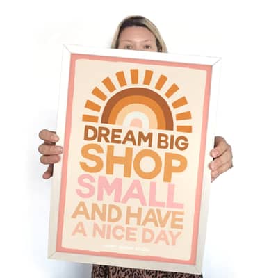 fabric banner hung next to a retro cabinet with a sunburst at the top and the words "DREAM BIG SHOP SMALL AND HAVE A NICE DAY" underneath in oranges and pinks