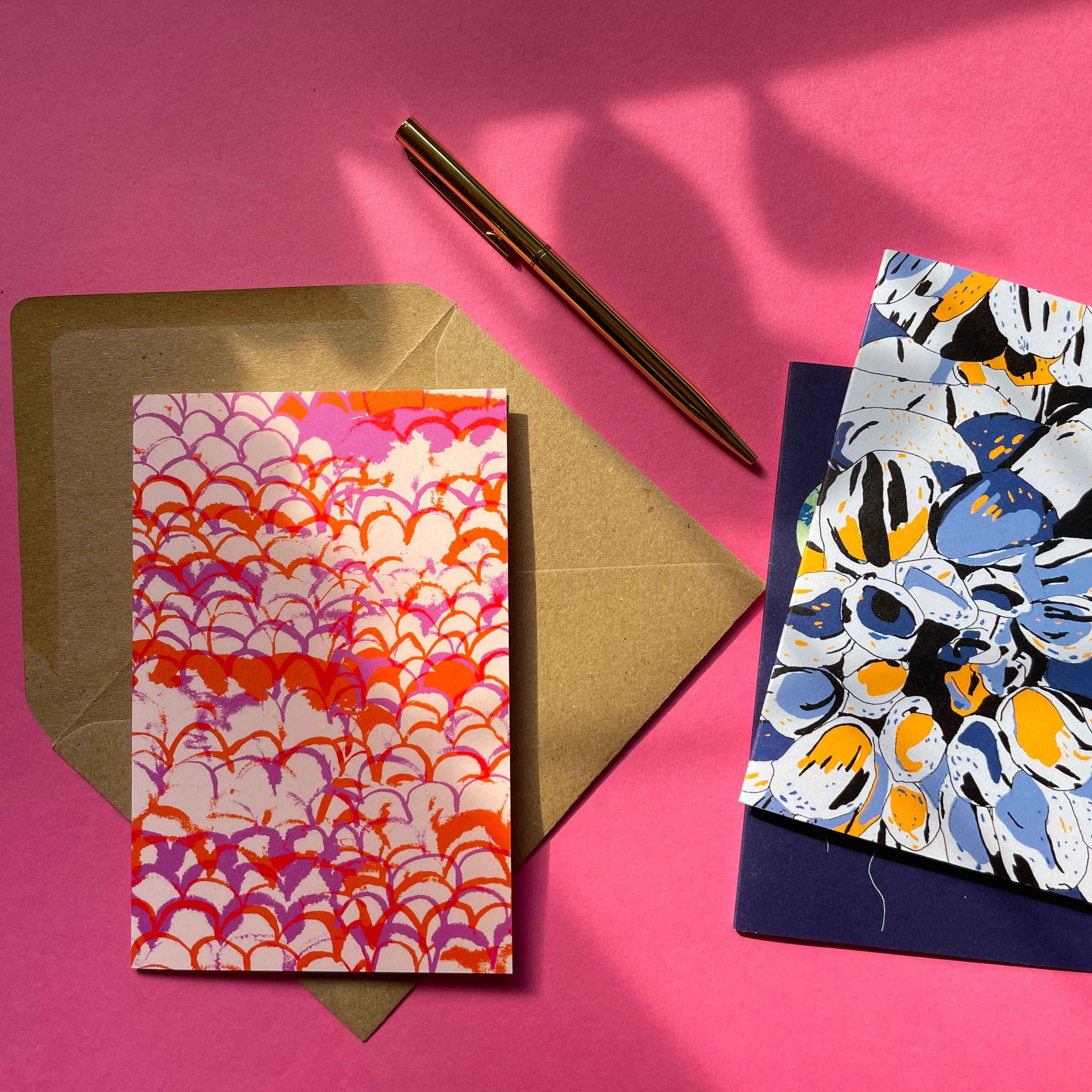 A pile of patterned A5 hardcover OlaOla notebooks with assoicated artwork and a silk stain headband.