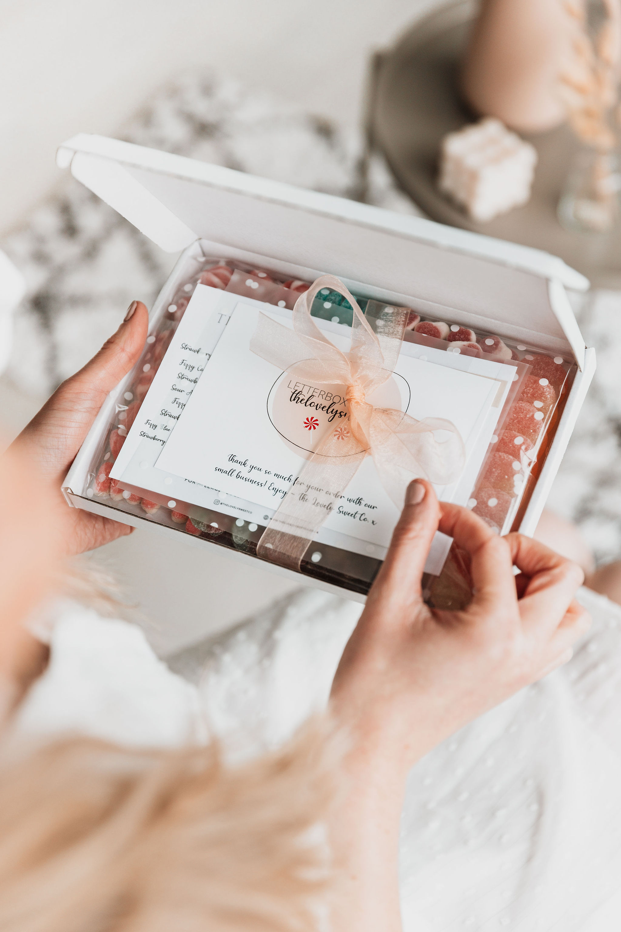 Our signature letterbox open, with a hand pulling on the peach ribbon to reveal the contents inside