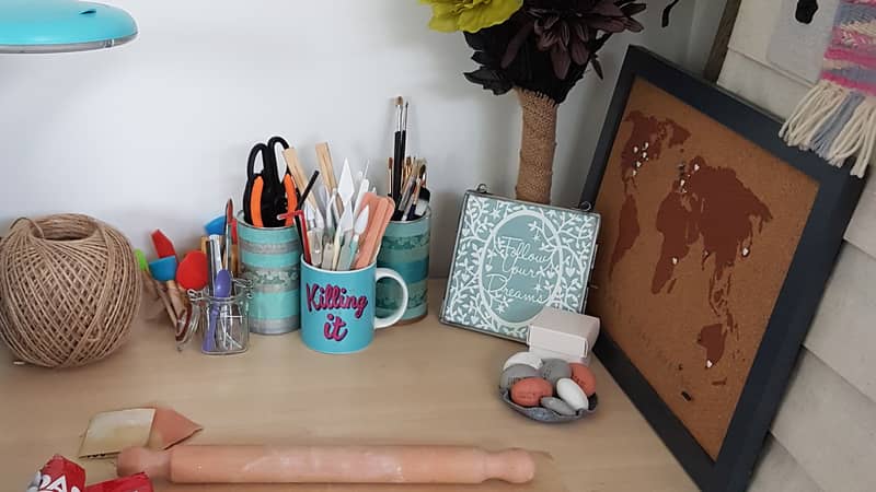 A picture showing a desk in Seema's work area. It has a pack of open clay, a rolling pin and cups of various tools.
