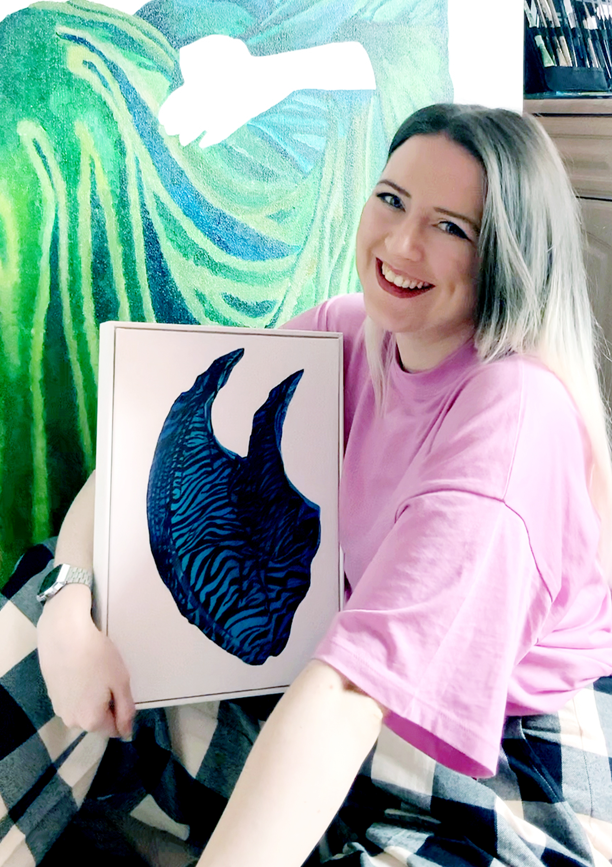 Kate Carter sits holding Wave, from her Absence of Figure series, in front of an acrylic self-portrait painting
