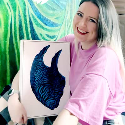 Kate Carter sits holding Wave, from her Absence of Figure series, in front of an acrylic self-portrait painting