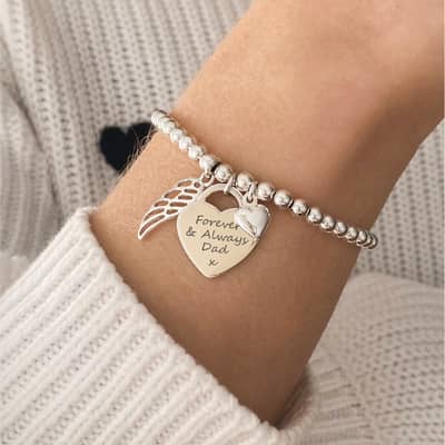 A silver charm bracelet worn on a model wearing a white jumper