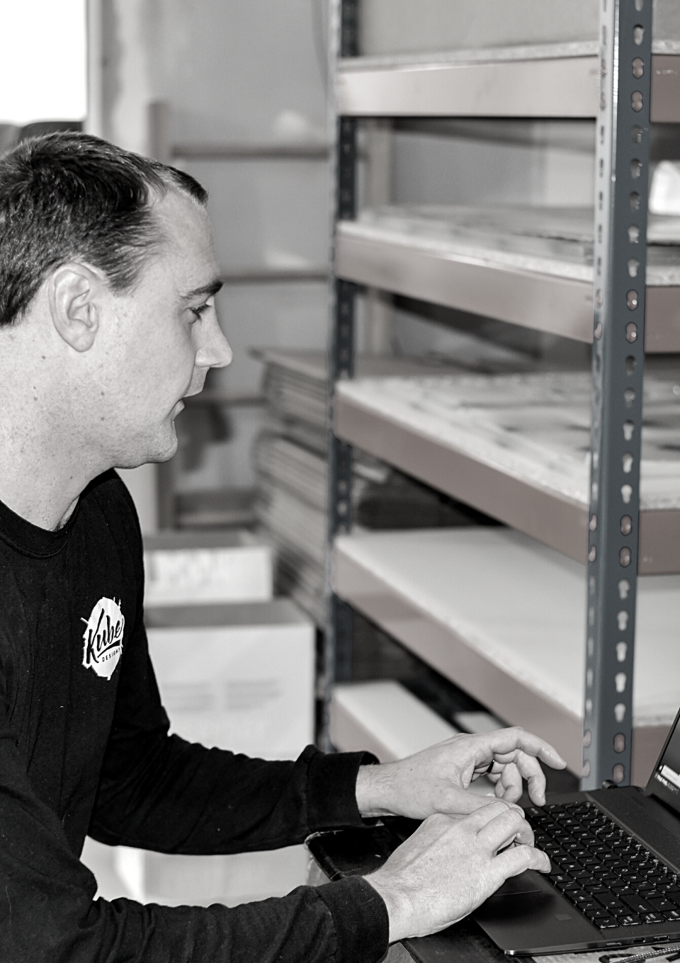 Darryl working at a computer with acrylic stored in background