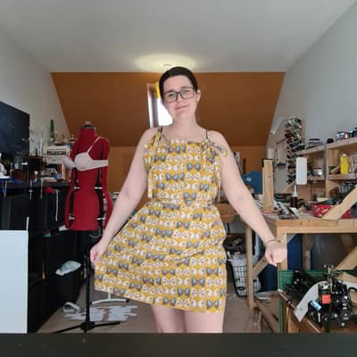 Image shows the maker in a handmade dress in the sewing room - dress is yellow with butterfly's