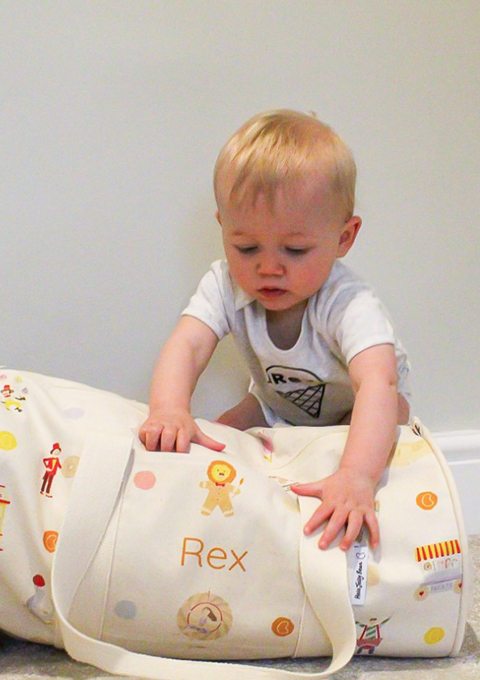 Toddler reaches for a Hele Jelly Bean personalised circus print overnight bag made from organic cotton.