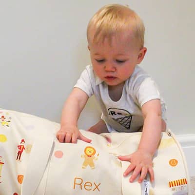 Toddler reaches for a Hele Jelly Bean personalised circus print overnight bag made from organic cotton.