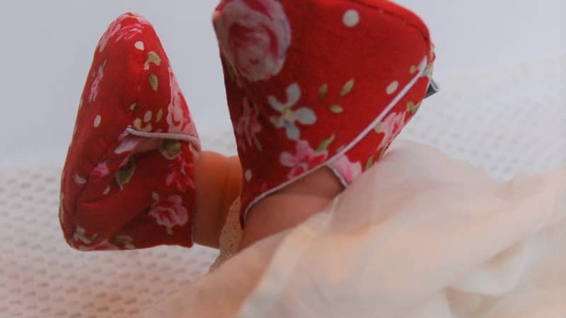 a pair of baby slippers on a baby's feet in a red floral pattern