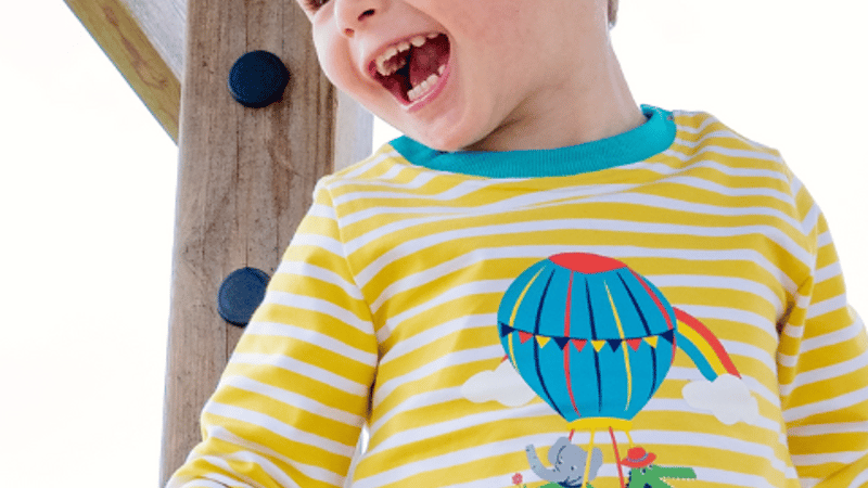 Image of a happy boy wearing a yellow and white stripe Ducky Zebra top with an elephant and crocodile in a hot air ballon