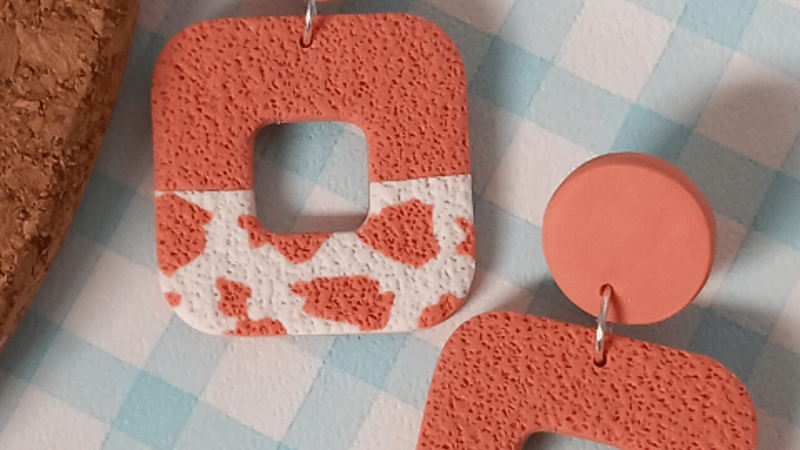 Coral pink textured polymer clay earrings with a cow print pattern