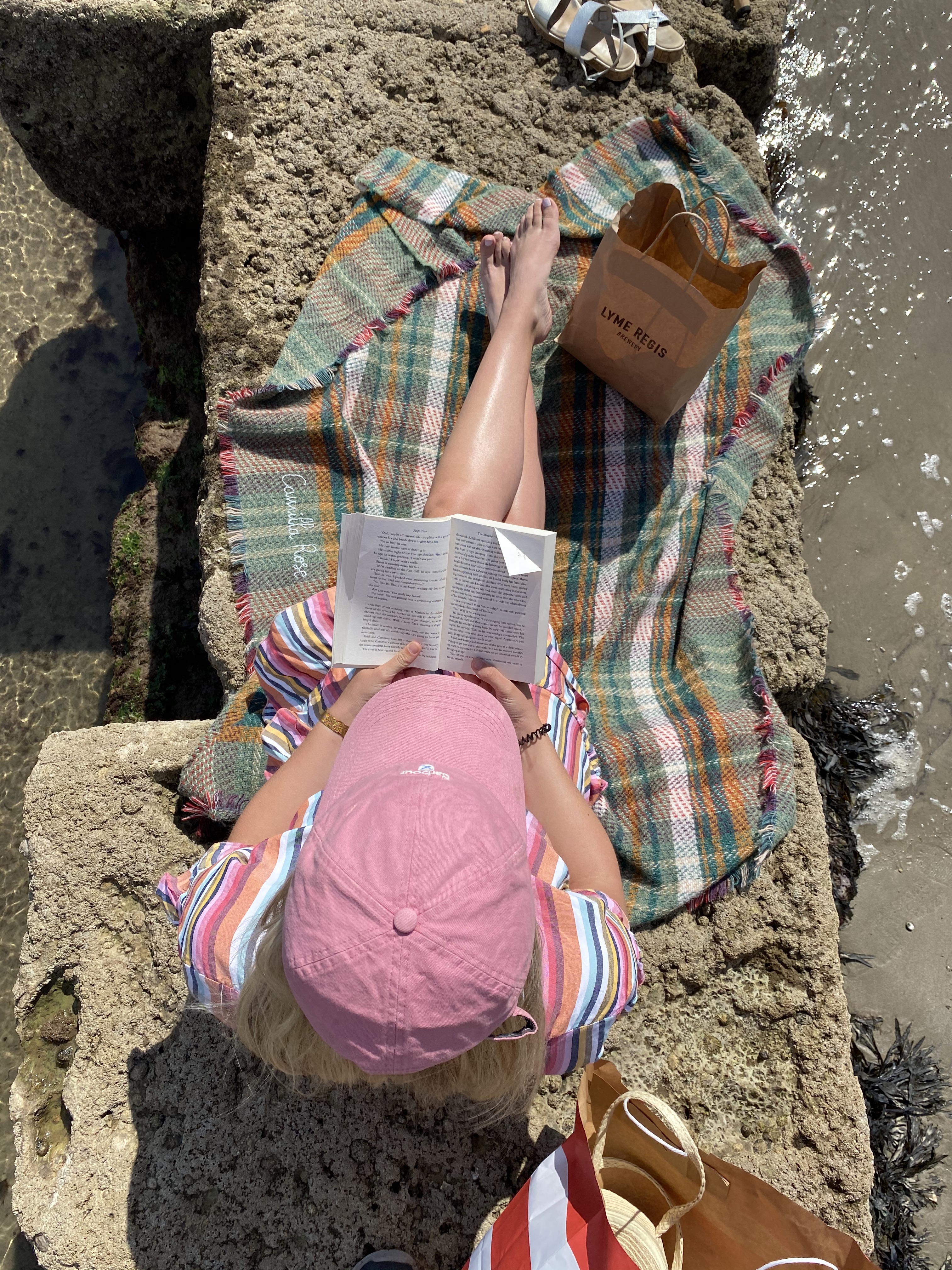 Woman sitting on blanket on seafront wall reading a book