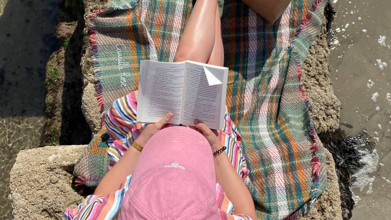 Woman sitting on blanket on seafront wall reading a book