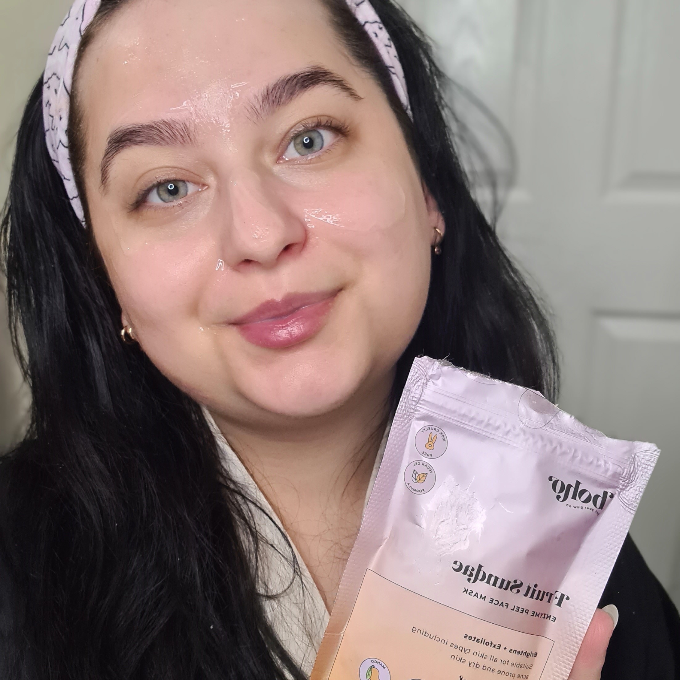 a lady with black hair and pink head band holding a pink pouch that contains face mask