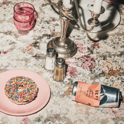 A crushed can of DEFY organic rosé wine on a table next to a doughnut.