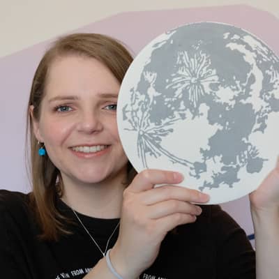 A white woman holding up a handmade jesmonite moon by Astral Tides