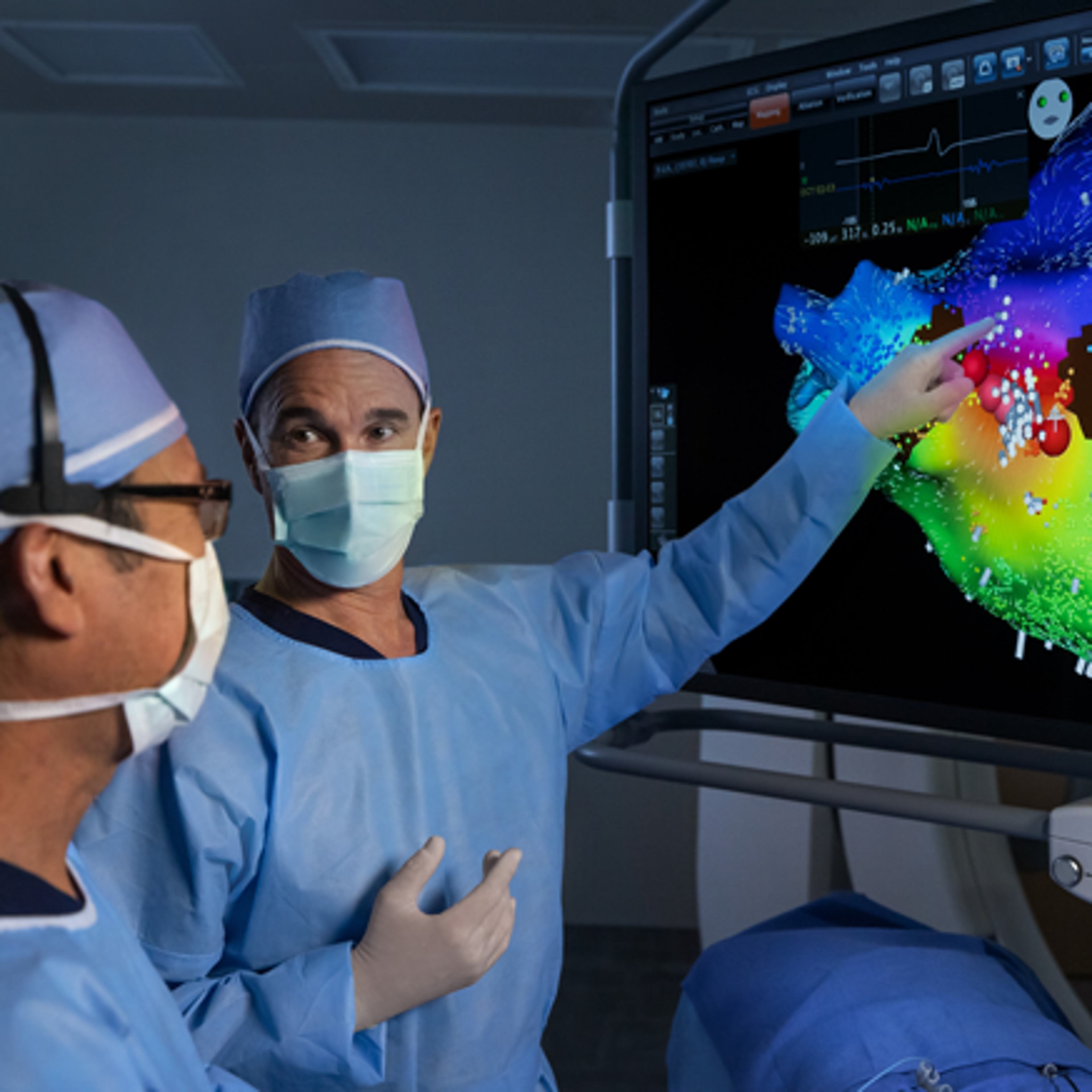 Two clinicians in the electrophysiology lab reviewing a colorful 3D cardiac mapping display on the CARTO™ System, with one clinician pointing to marked activation points on the screen.