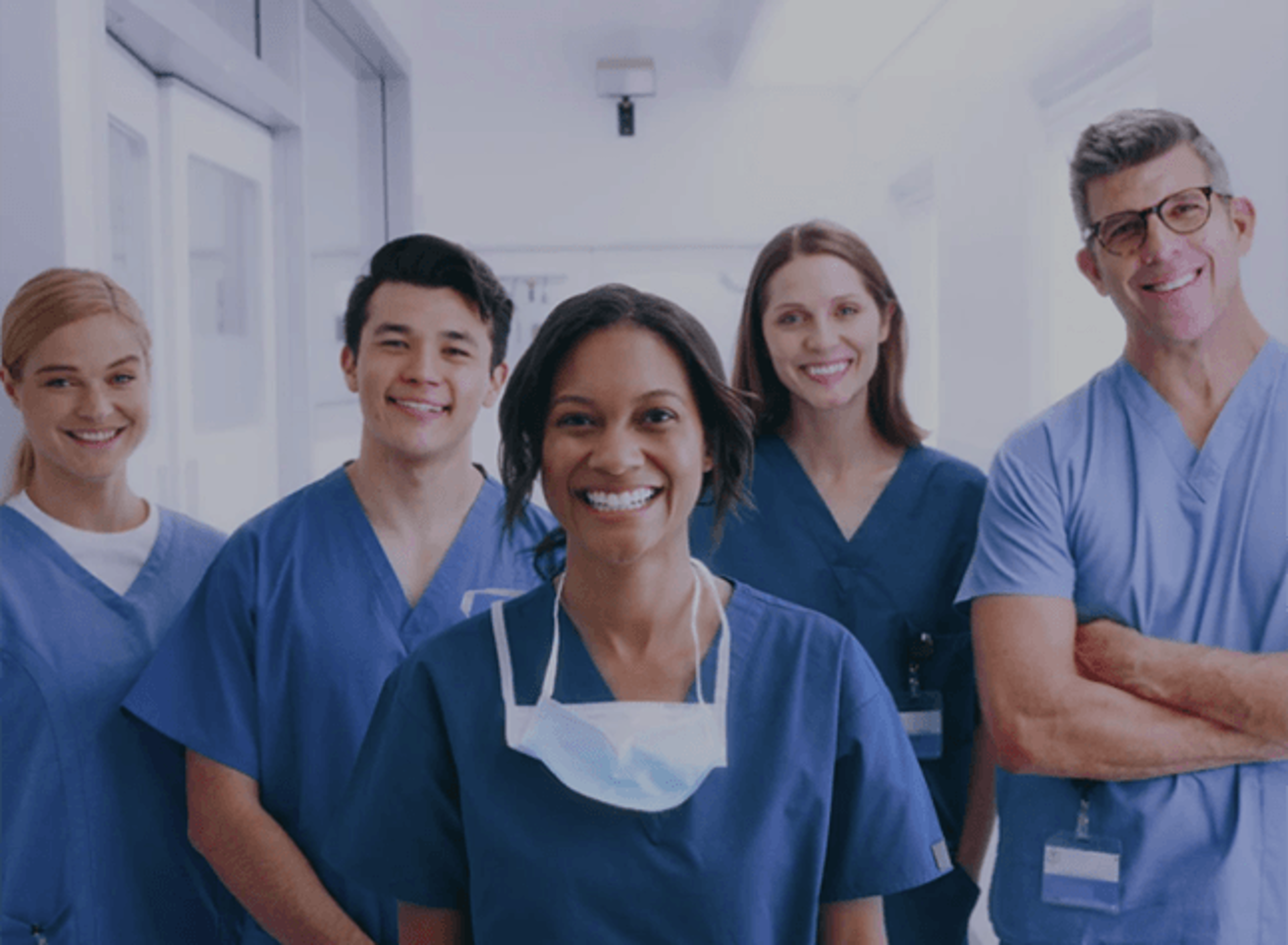 Five healthcare professionals wearing blue medical scrubs standing together in a bright hallway