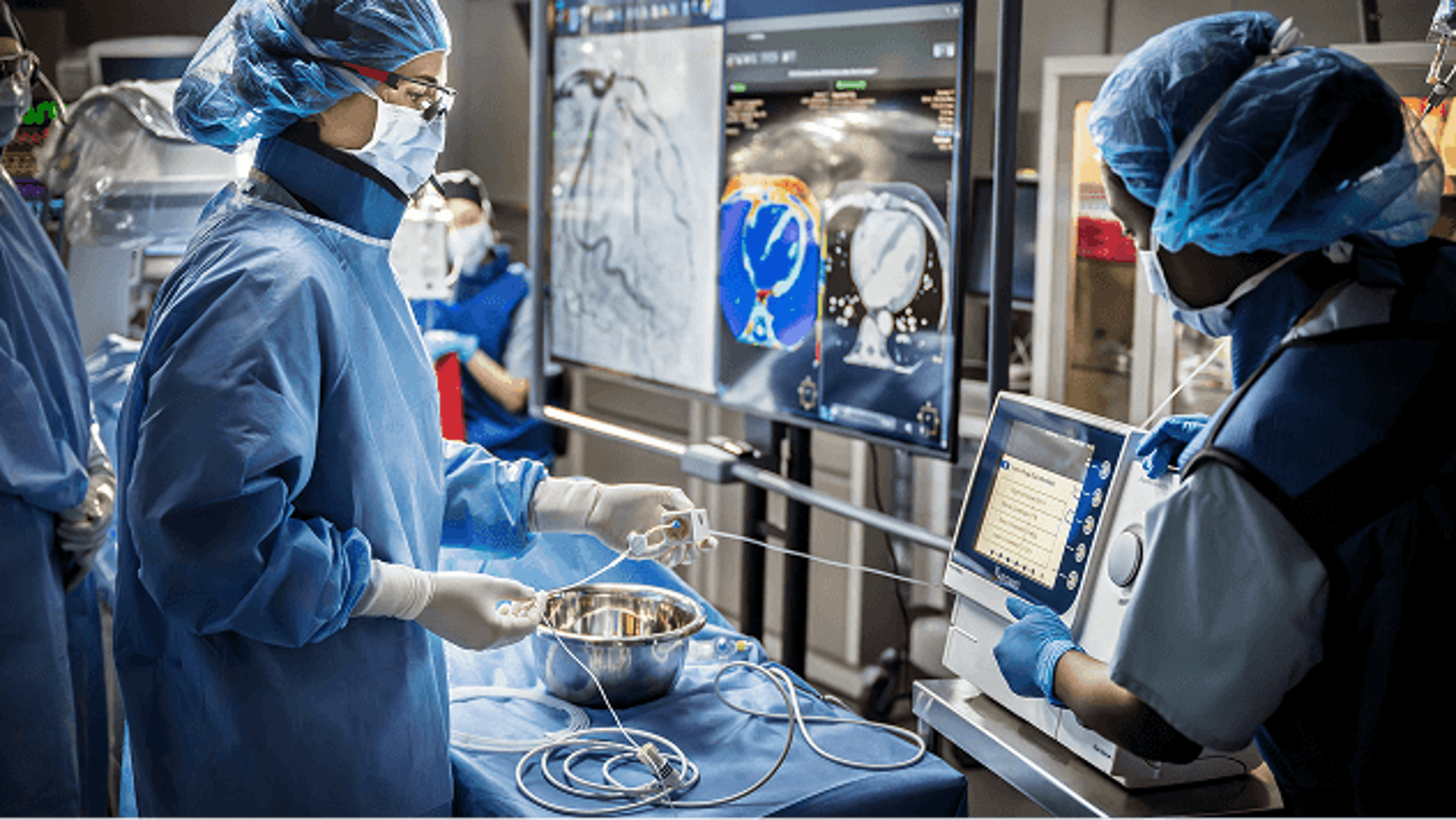 Scrub technician and circulating nurse prepare the Impella heart pump console during an endovascular procedure, with imaging monitors and sterile instruments visible in the operating room.