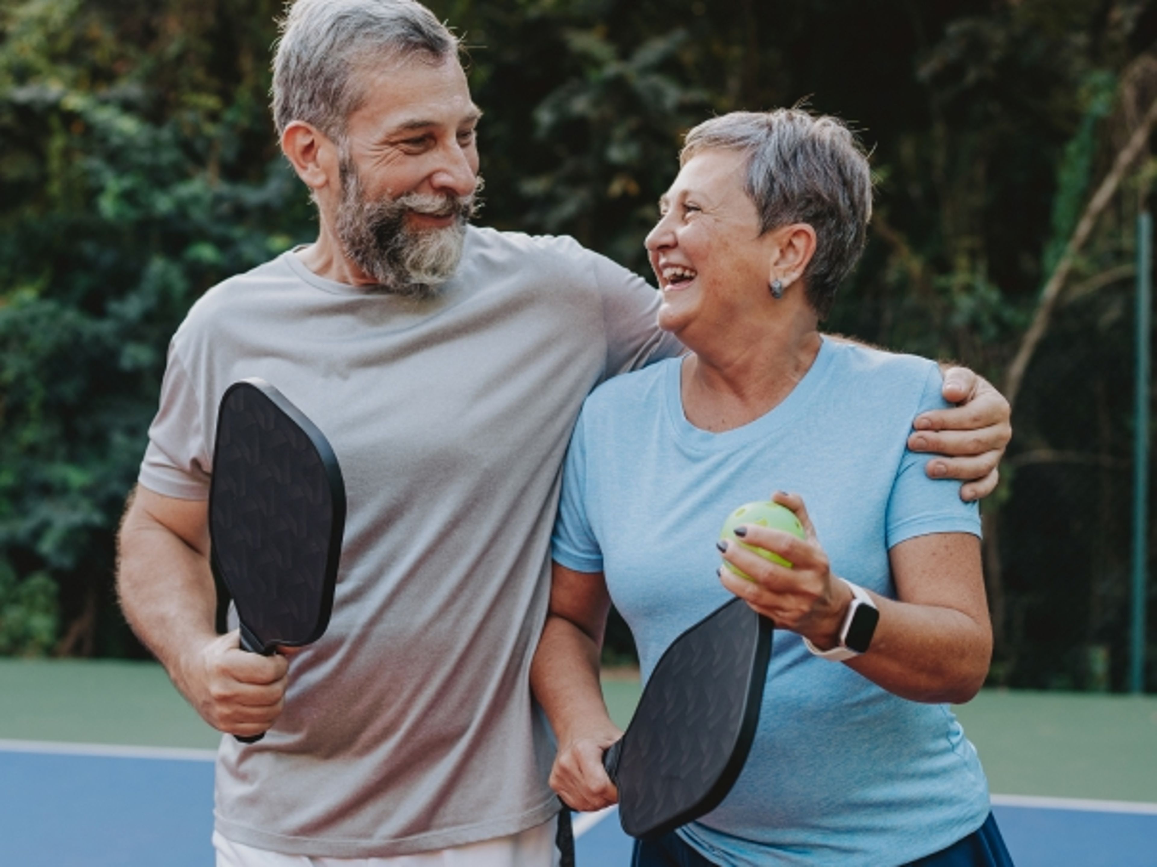 Older couple holding pickleball paddles on a court