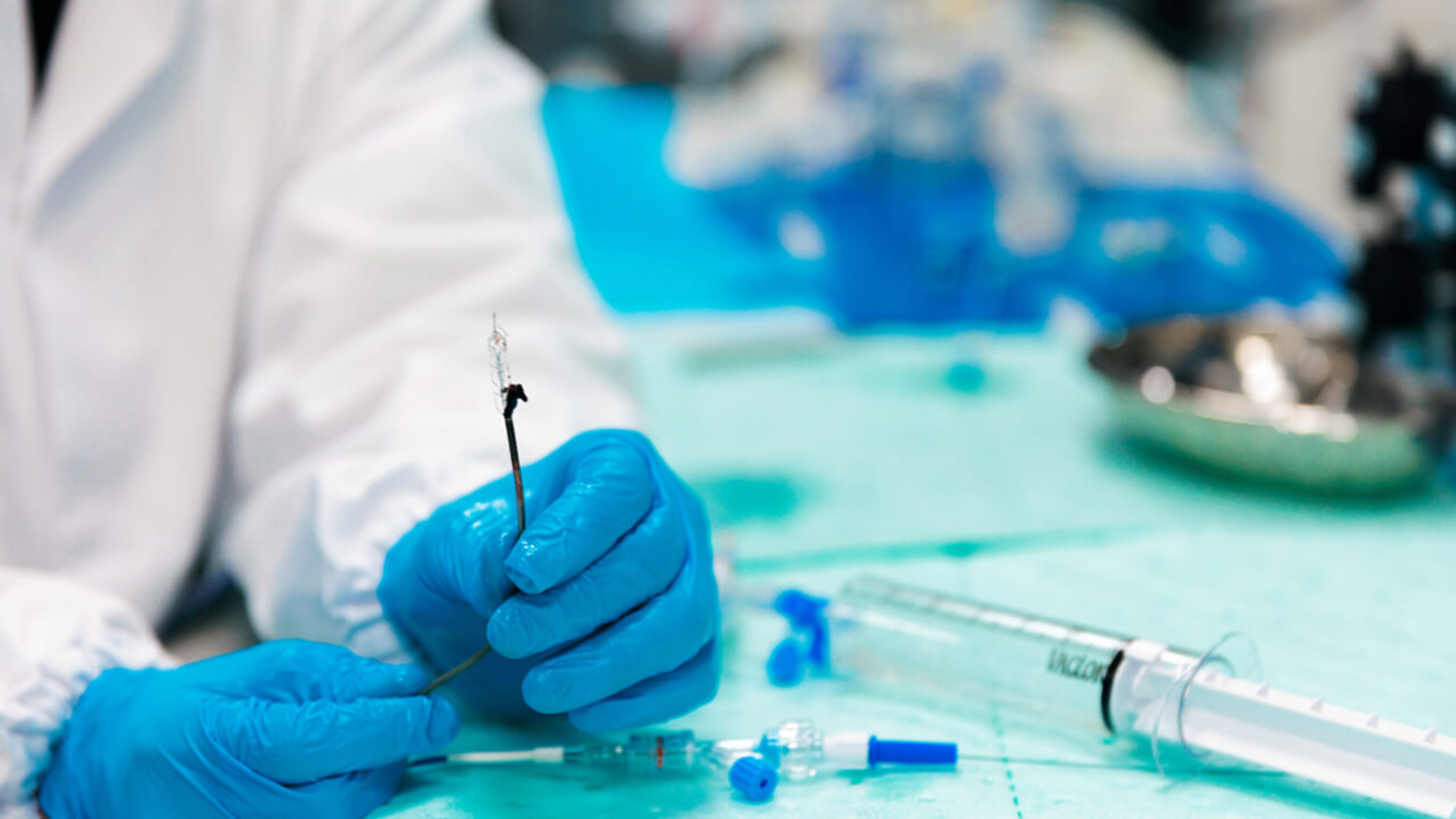 A scientist with blue gloves holding a medical device