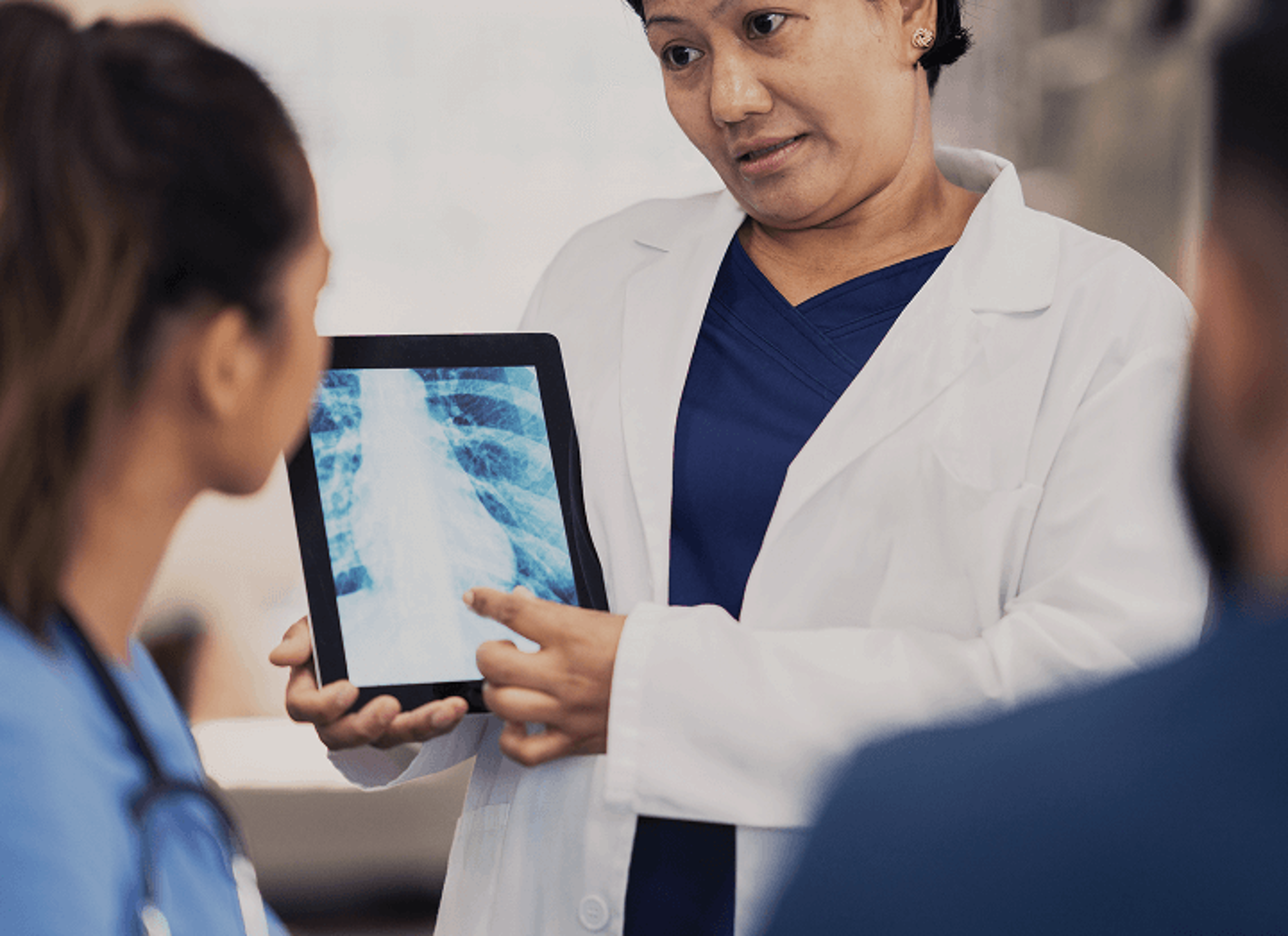 Healthcare professional showing a chest X‑ray on a tablet to two patients during a consultation.
