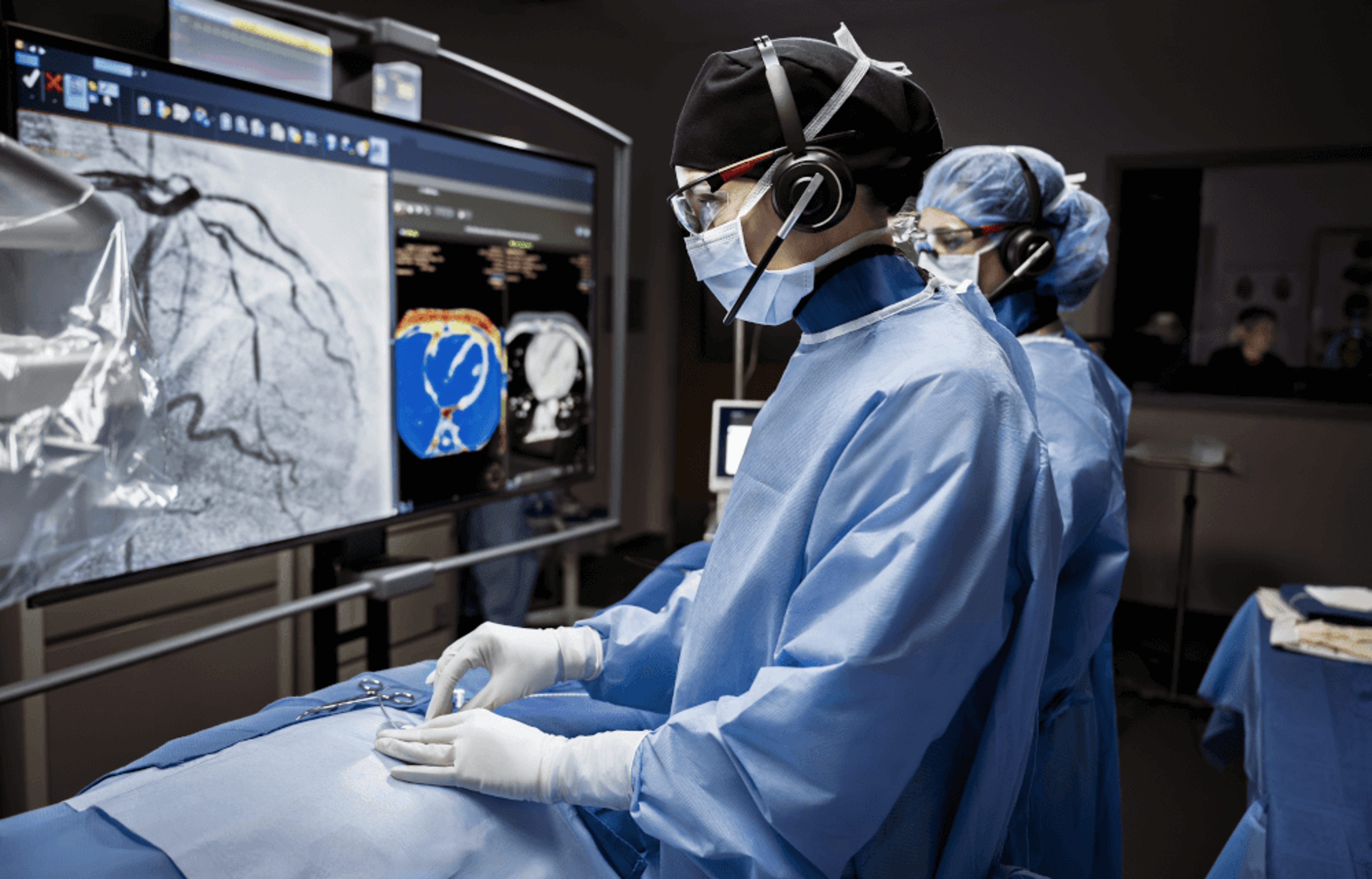 Clinicians in the cath lab perform an endovascular procedure using an Impella heart pump, with the control room team visible in the background monitoring the case.