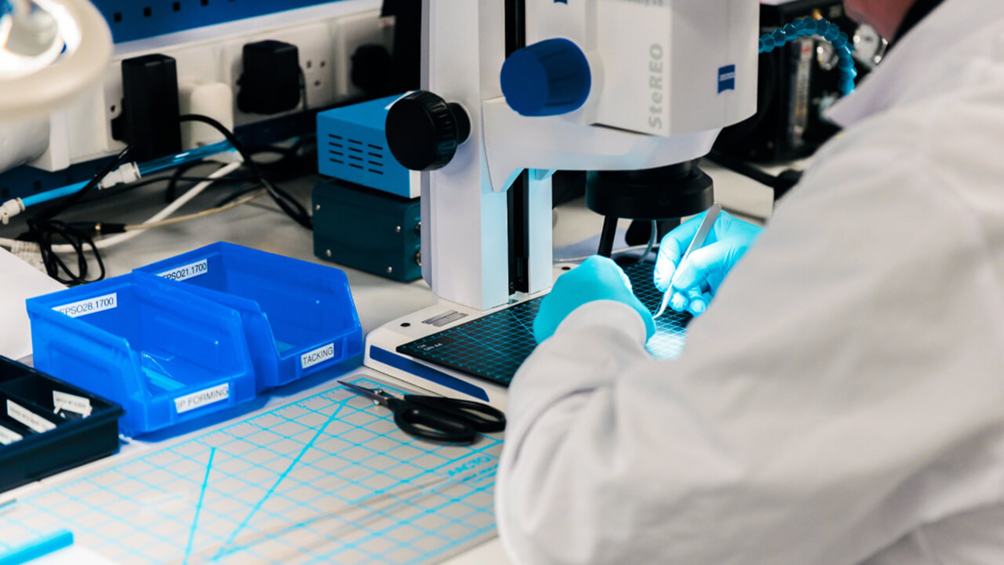 A scientist with blue gloves working on a medical device using a dissecting microscope