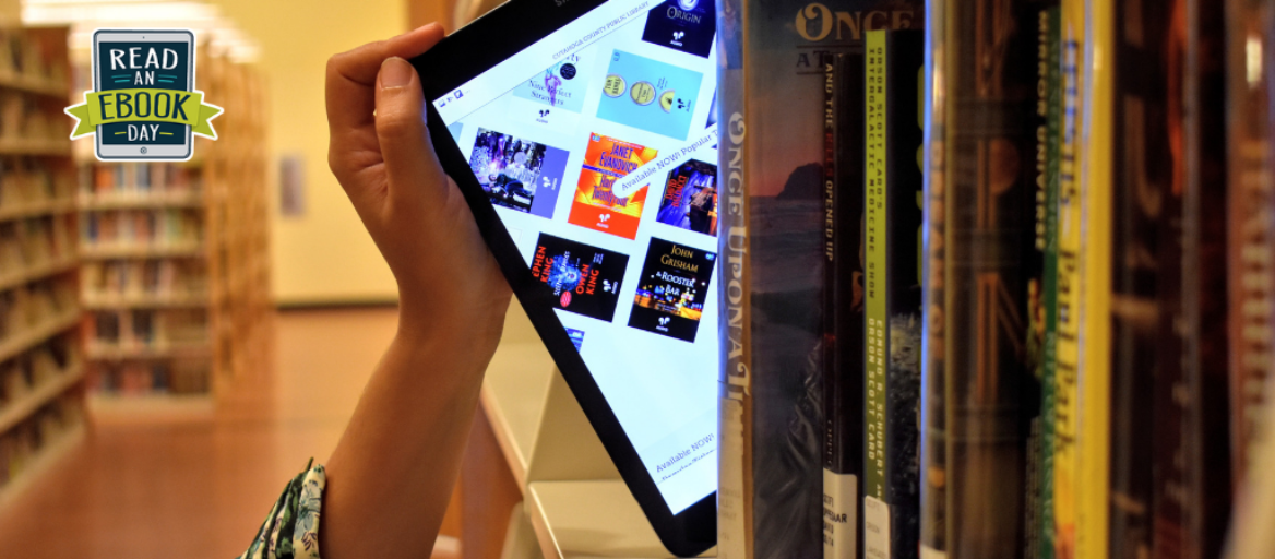 A hand pulls a tablet featuring the Libby app off of a library bookshelf.