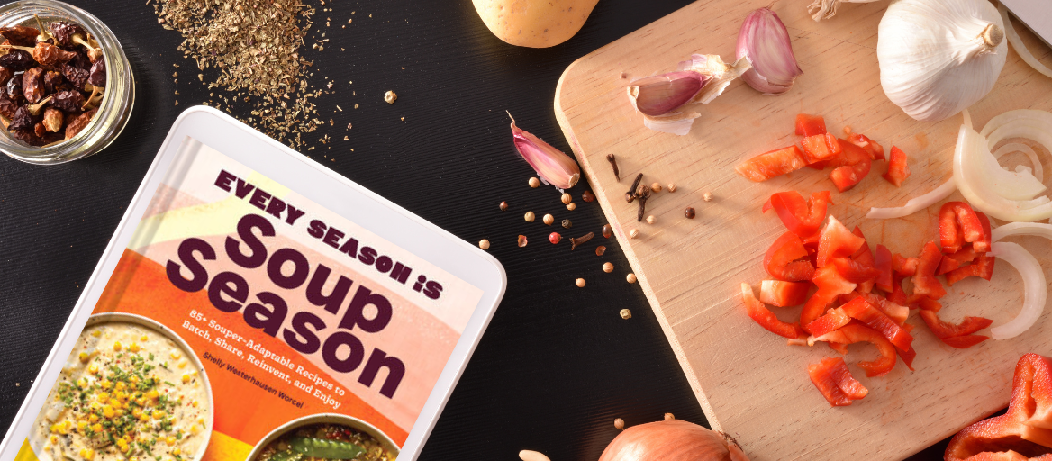 A cutting board with vegetables and spices and a tablet with the ebook "Every Season is Soup Season."