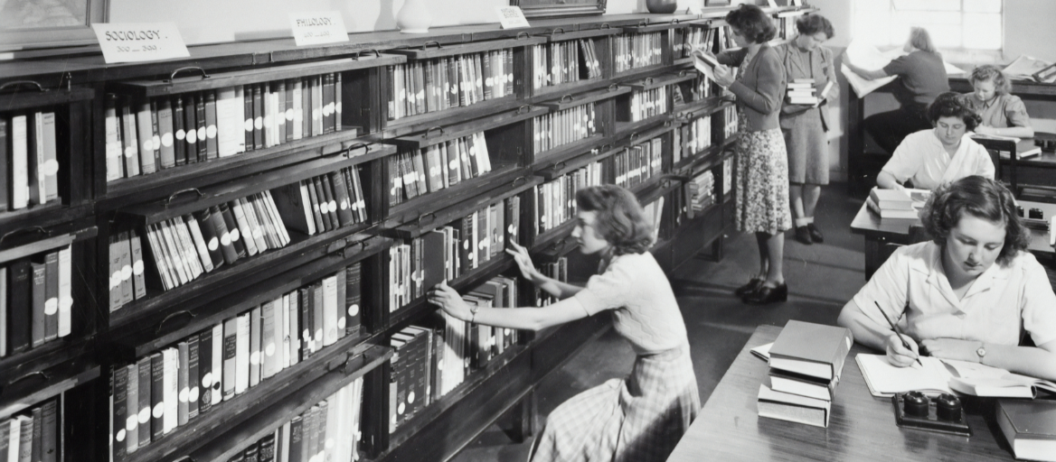 Black-and-white vintage photograph of patrons browsing books at the library and working at tables