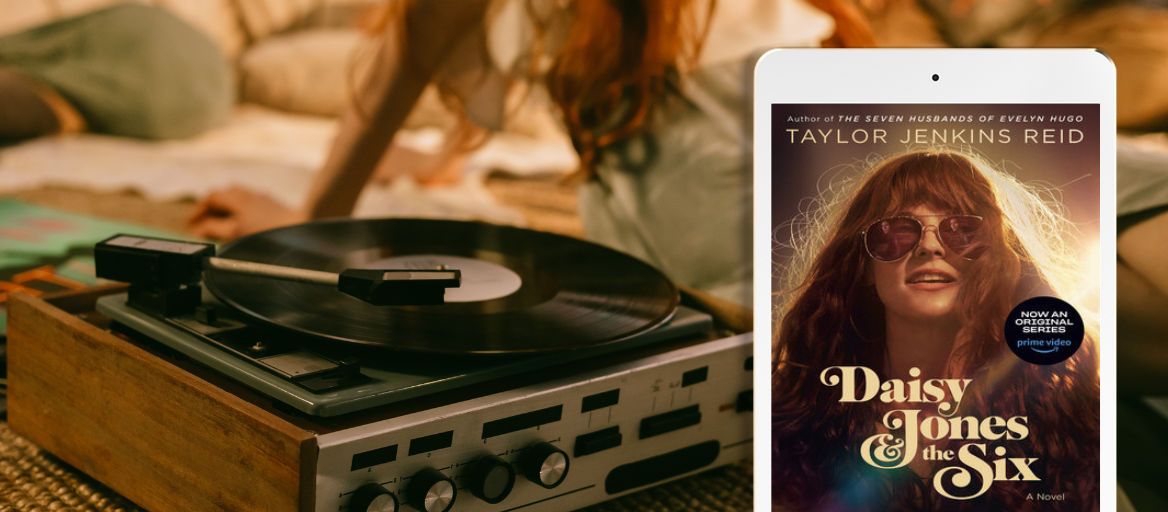 A record player sits on a bed next to a girl with long red hair in the background. A white tablet features the cover of "Daisy Jones and the Six."