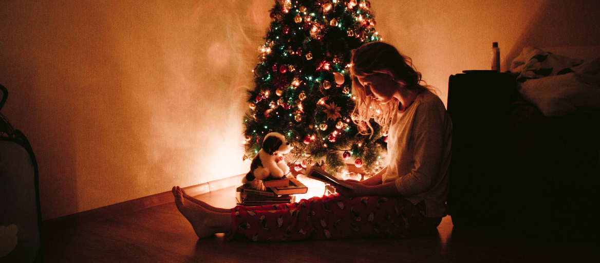Person sitting on the floor reading under a lighted Christmas tree