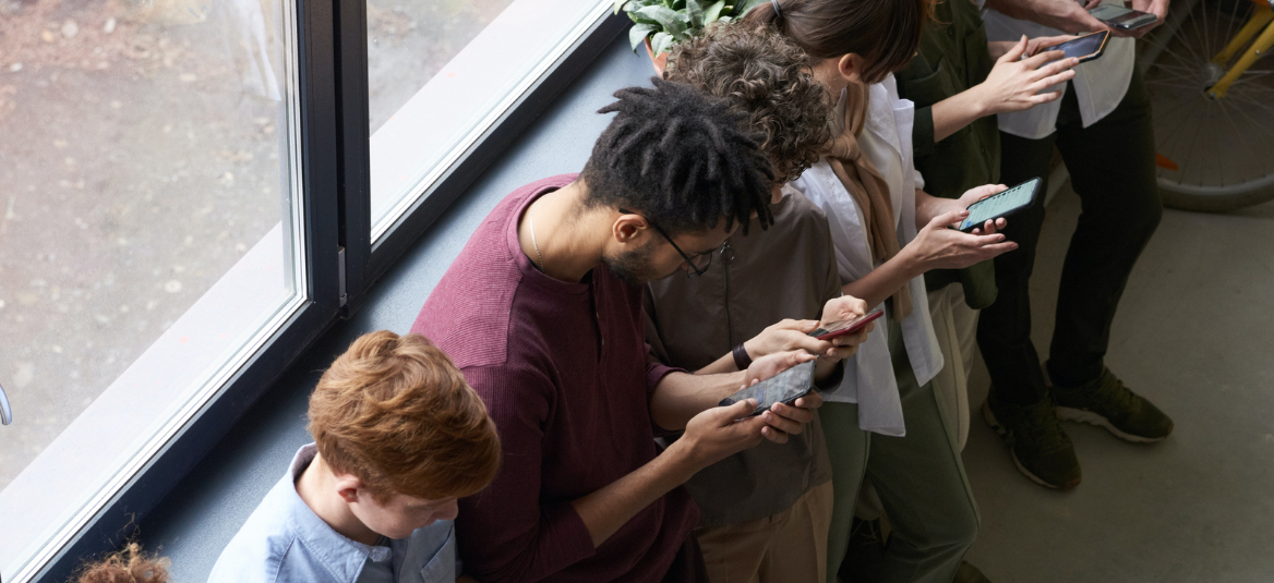 Group of people standing in front of a window looking at their phones