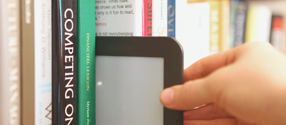 An ebook reader is being pulled off a shelf with physical books