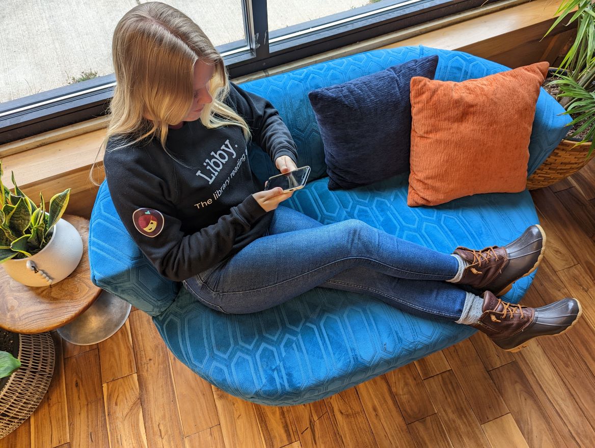Person reading on a blue couch wearing a black Libby sweatshirt