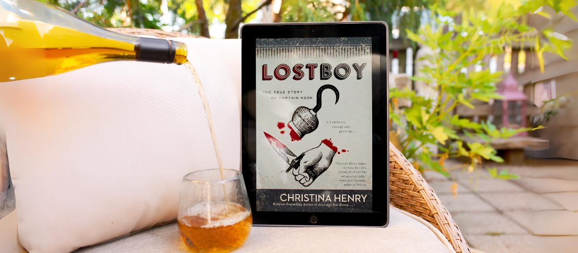 A glass of wine being poured on a porch next to a tablet featuring the ebook "Lost Boy."