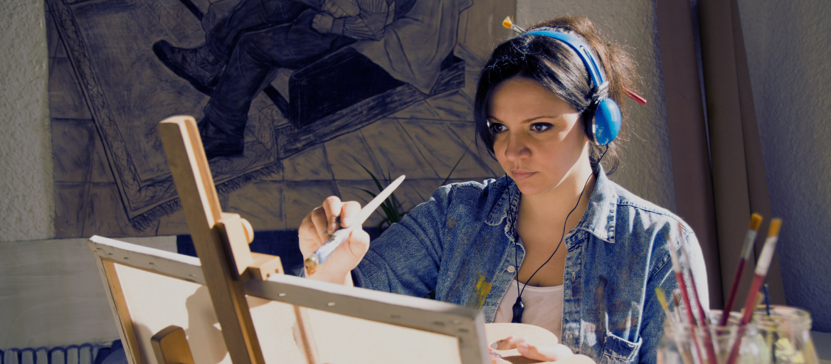 A woman paints on a canvas while wearing headphones