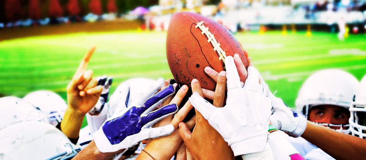 A group of football players with their hands on top of each other holding a football