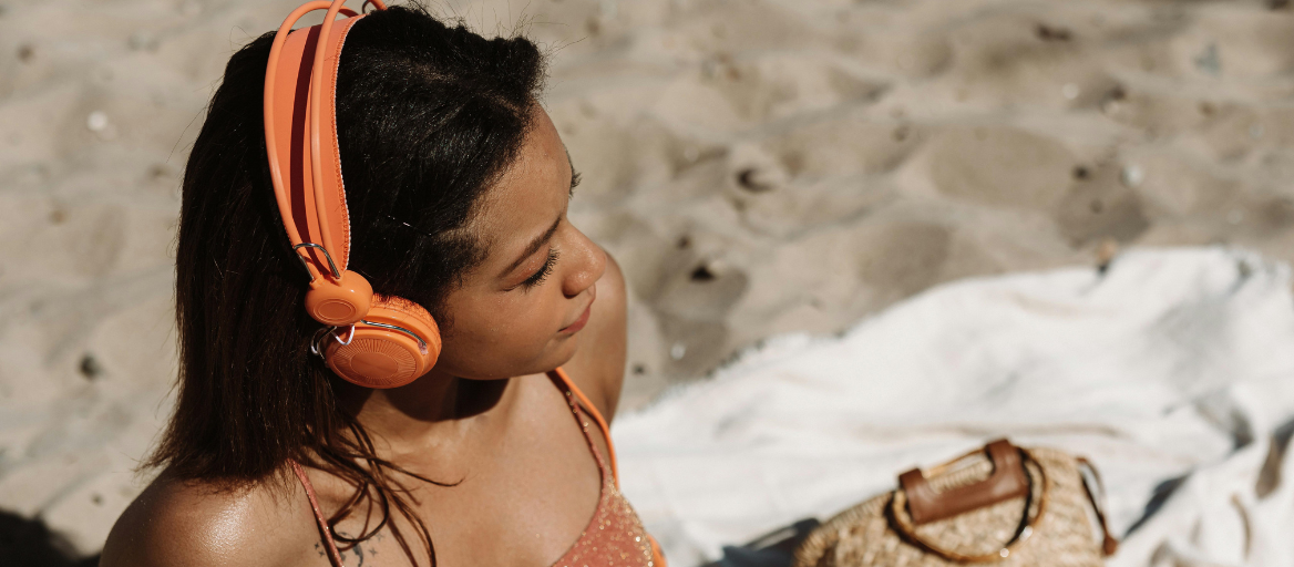 A woman relaxes at the beach with orange headphones