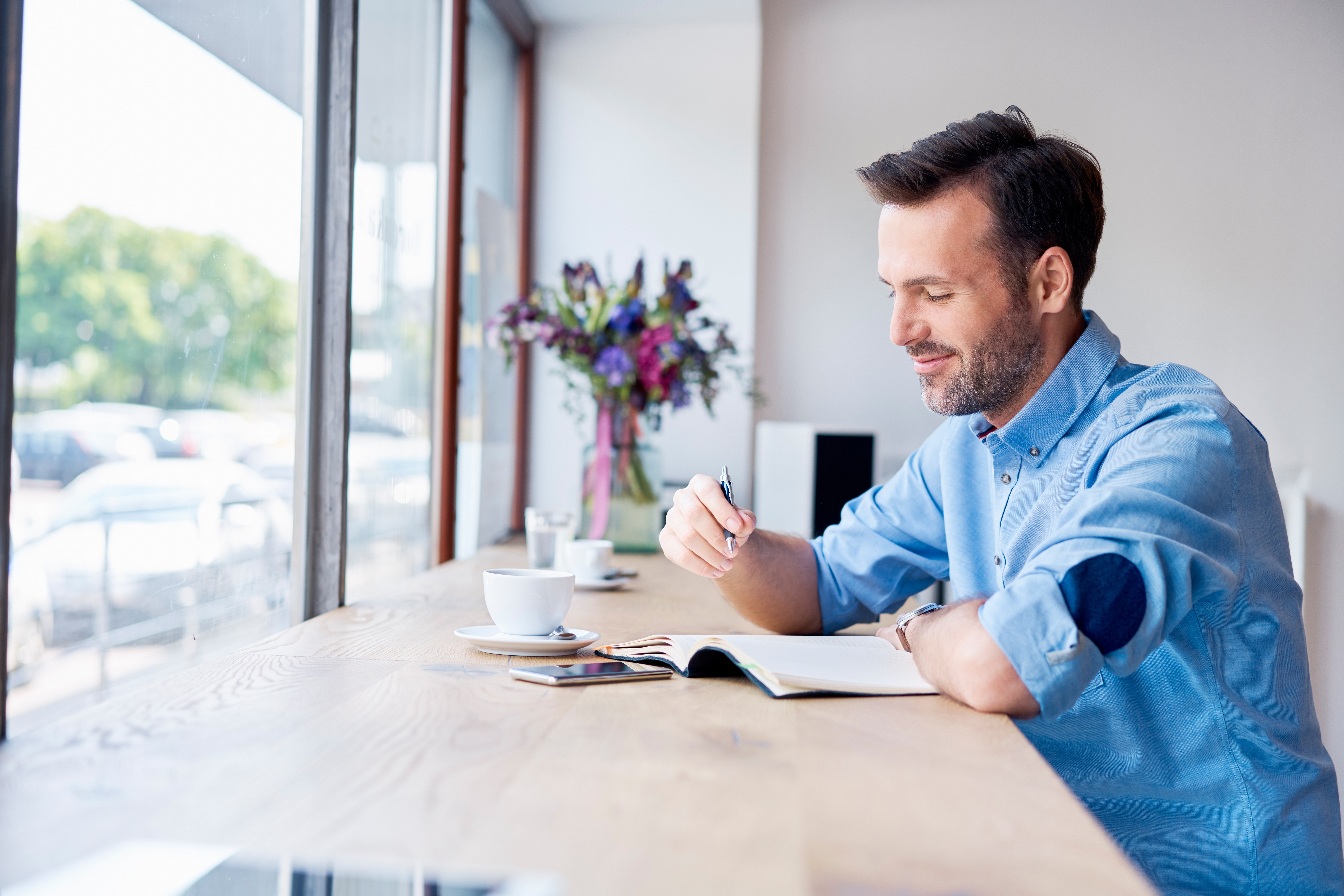 Man in a coffee shop writing notes in his diary.