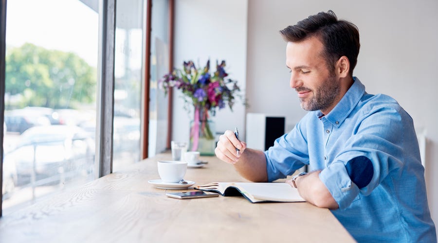 Man in a coffee shop writing notes in his diary.