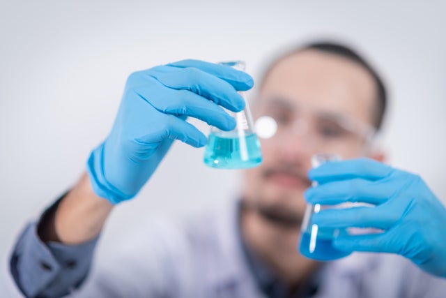 044_person_in_latex_gloves_comparing_two_flasks_with_blue_liquid.jpg