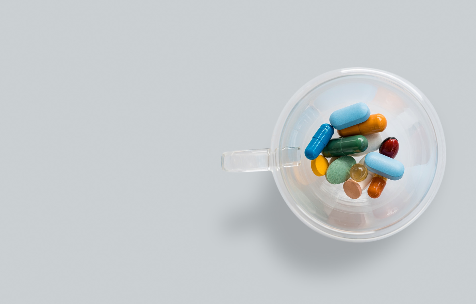 various colorful pills in glass cup on white table