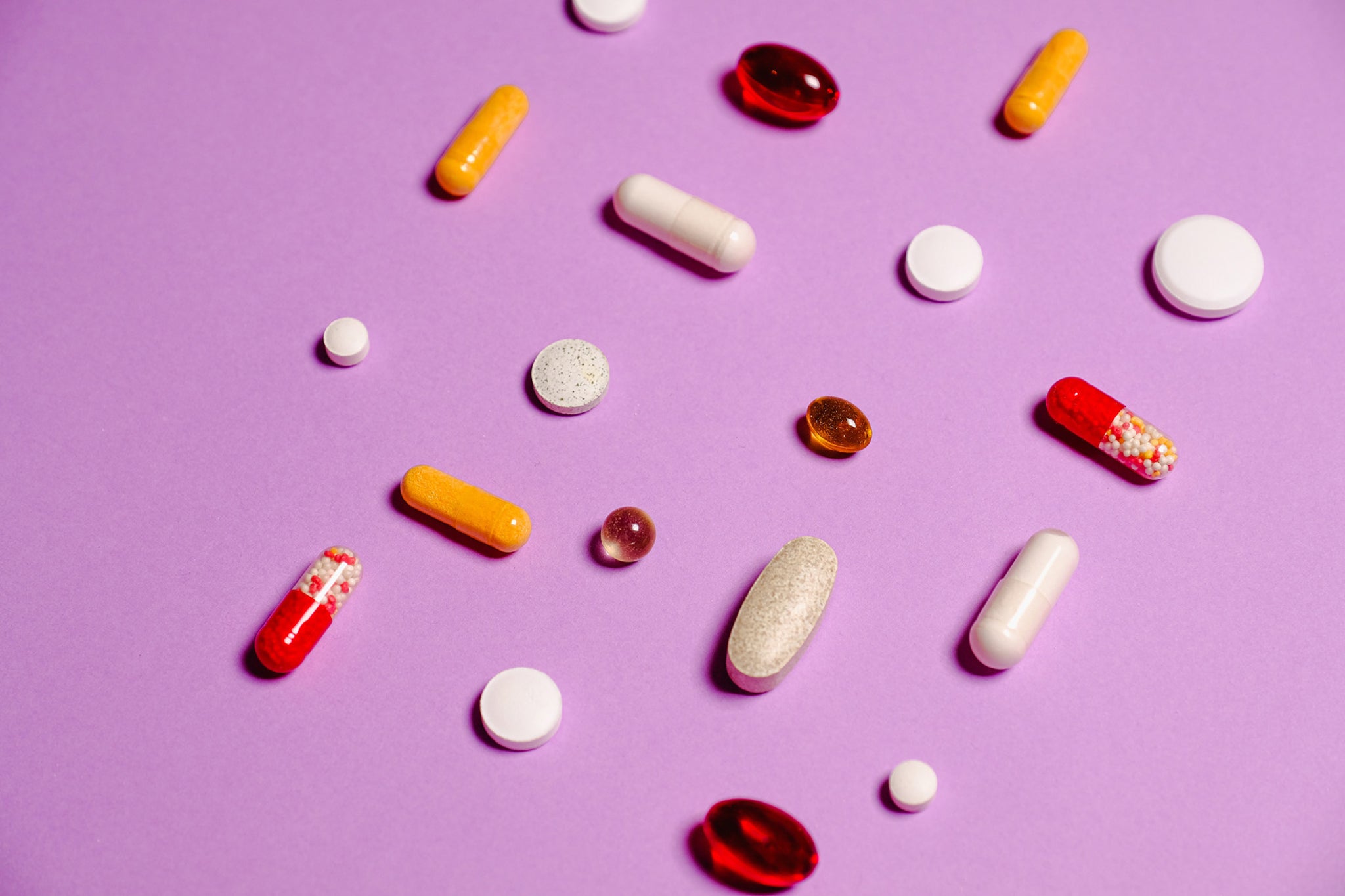 assorted pills and capsules on a pink background
