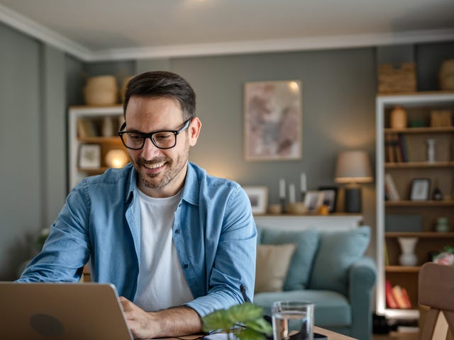 Man sitting at a table in his living room and looking for online language courses on his laptop