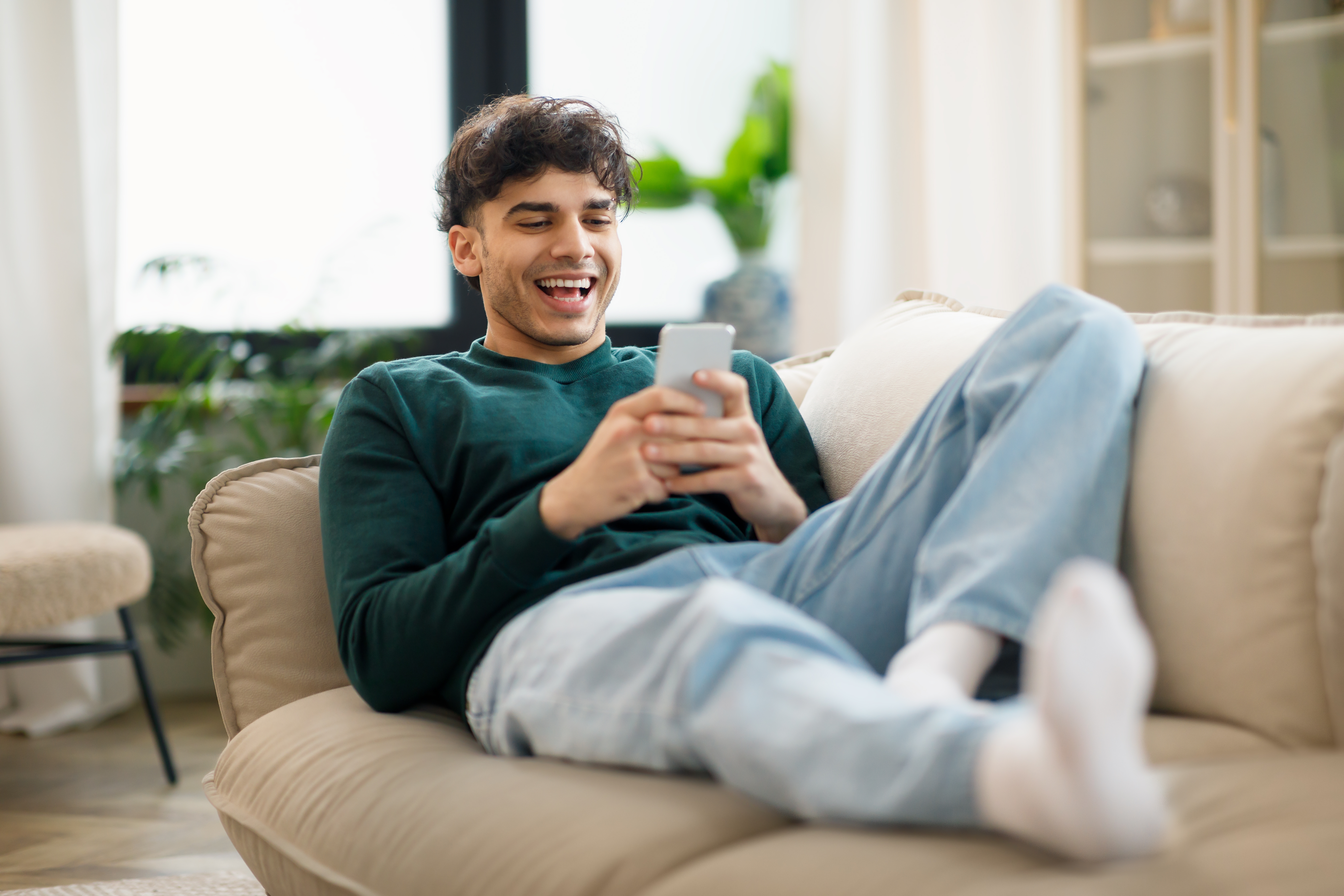 Man sitting on a couch holding his phone and learning a language with Berlitz Flex