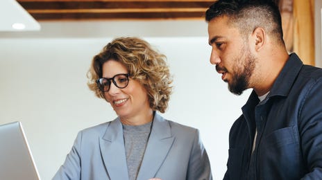 Student and instructor standing at a table and looking at a laptop and talking to each other during a language immersion program