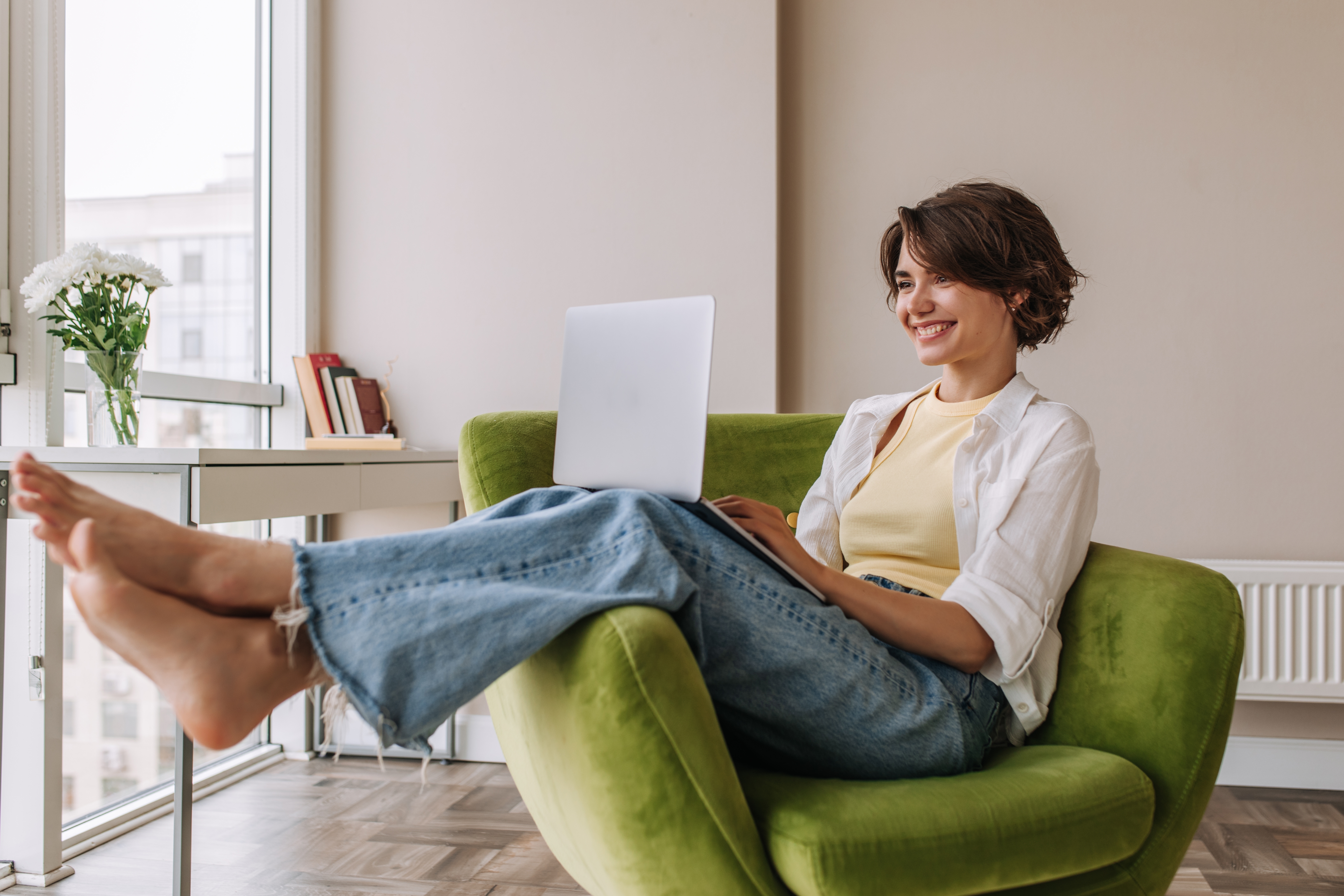Woman sitting in an armchair with a laptop in her lap and smiling during an online group language lesson